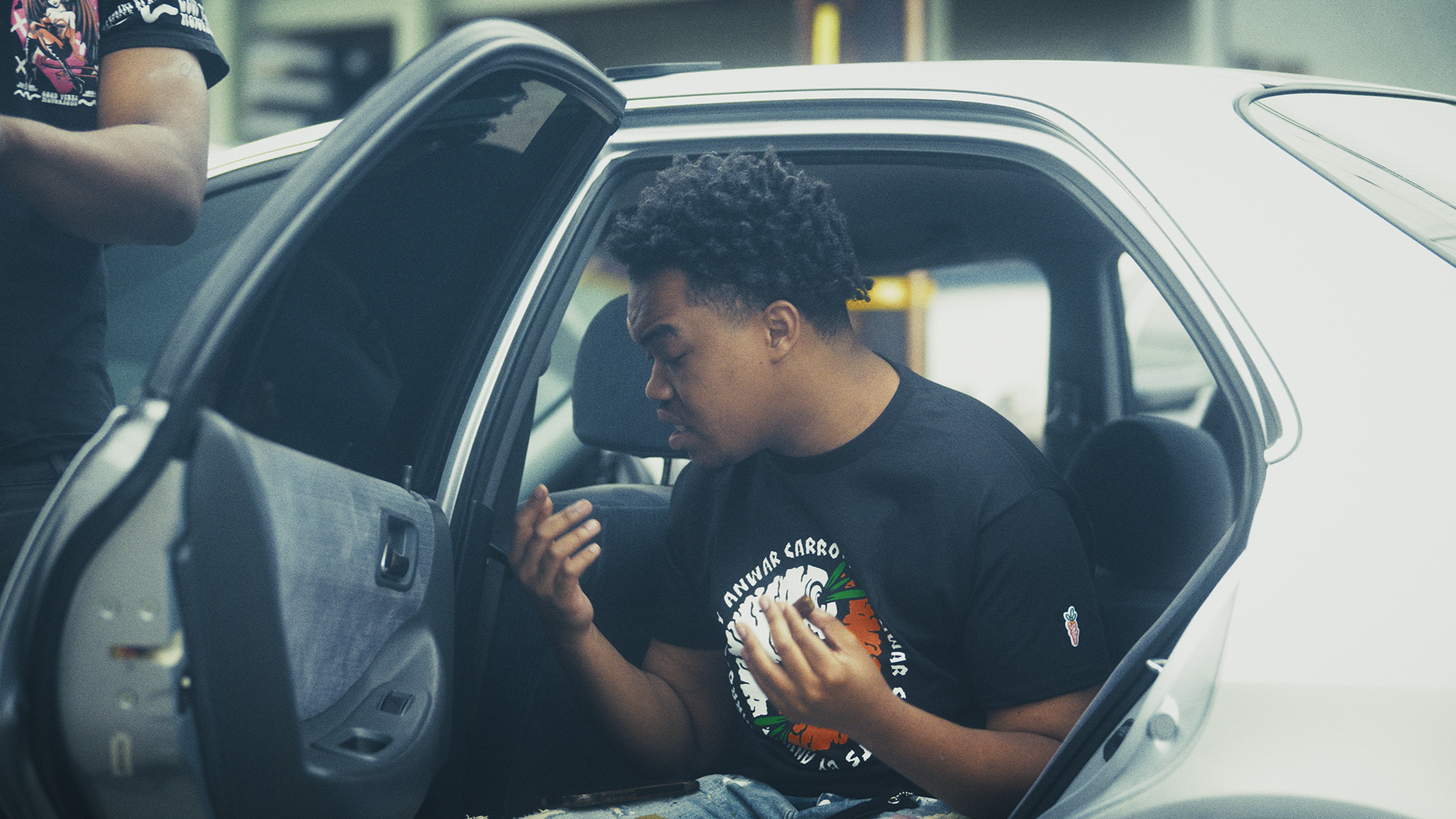 Music video still with artist seated in a car